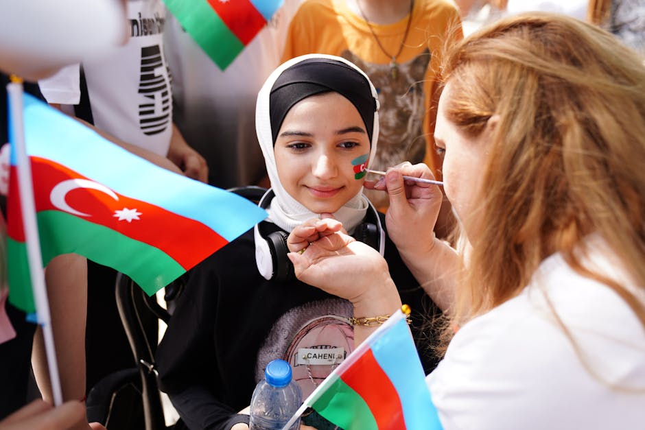 A girl gets her face painted with a flag at a lively outdoor gathering, holding an Azerbaijani flag.